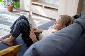 A girl with bright and lush blonde hair finds joy in reading a fascinating book, sitting on the...