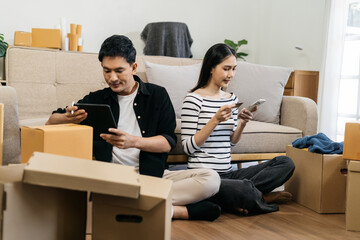 Young couple relaxing sitting on the sofa using the computer laptop around cardboard boxes, very happy moving to a new house.