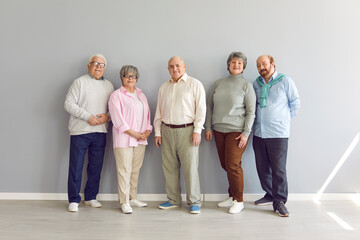 Group portrait of senior family members or friends. Several elderly people standing by wall. Retired old men and women in smart casual clothes standing together by grey wall. Older generation concept