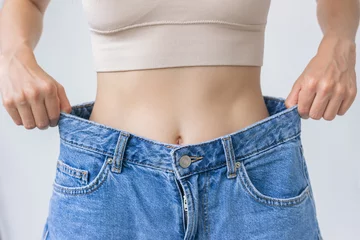 Fotobehang A young woman tries on jeans after a healthy weight loss, shows how big they turned out to be after. The concept of a healthy lifestyle and proper nutrition. © Ольга Шефер