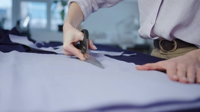 A seamstress woman cuts out a pattern with tailor's scissors, hands close-up