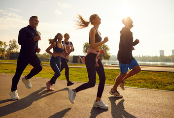 Group of sporty smiling people in sportswear jogging together in the park at sunset. Friends...