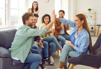 Portrait of a group of happy young friends students or coworkers giving high five reaching agreement sitting on sofa at home together. Young people men and women greeting each other. Teamwork concept