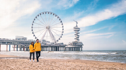 a couple of men and woman on the beach of Scheveningen Netherlands during Spring, The Ferris Wheel at The Pier at Scheveningen in the Netherlands, Sunny spring day at the beach of Holland - obrazy, fototapety, plakaty
