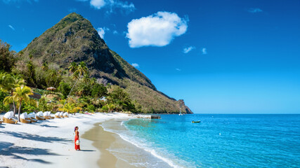 St Lucia Caribbean, woman on vacation at the tropical Island of Saint Lucia Caribbean ocean, an Asian woman in red dress walking on the beach - obrazy, fototapety, plakaty