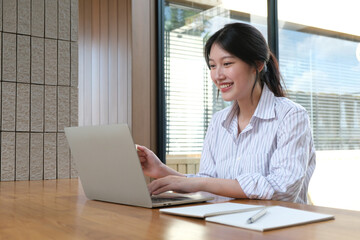 Smiling beautiful Asian businesswoman working on laptop and documents in financial accounting concept office