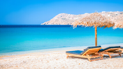 Mykonos beach during summer with umbrella and luxury beach chairs beds, blue ocean with a mountain...
