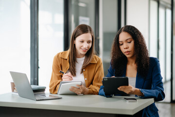 Two business workers talking on the smartphone tablet and using laptop at office...