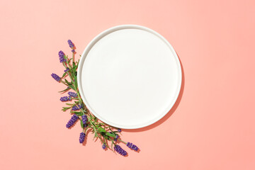 Lavender flowers are arranged around a round white ceramic plate on a pink background. Lavender...