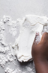 Hands kneading white fondant for decorating cake, fondant being mixed on a table
