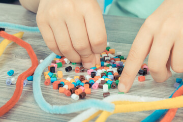 Preschooler hands with creative sticks and beads used to making bracelets. Development of kids...