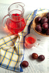 Plum Compote in jug with purple plums on white wooden background. .