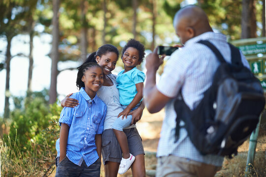 Smile, photograph and a black family hiking in the forest together for travel, tourism or adventure. Love, photography or memory with a man, woman and children in the woods or wilderness for freedom
