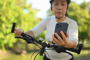 Senior woman hand using mobile phone checking route map location while riding exercise bicycle.