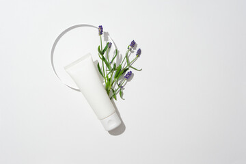 An empty tube and fresh lavender flowers are placed next to a round glass podium on a white...
