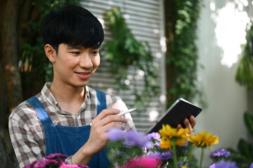 Portrait of happy Asian male florist in apron using digital tablet at small business flower shop.