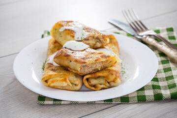 Thin fried pancakes with meat filling in a plate with sour cream and spices.