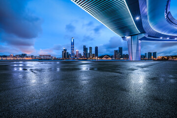 Asphalt road square and pedestrian bridge with city skyline at night