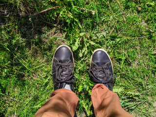 First person view of a man looking down at the shoes that are standing in the grass in the summer during the daytime.