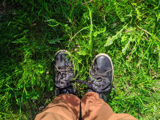 First person view of a man looking down at the shoes that are standing in the grass in the summer during the daytime.