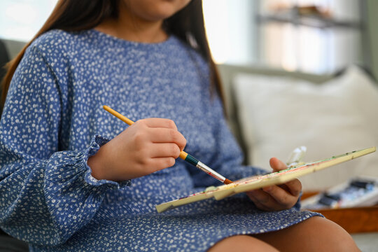 Cropped Shot Of Little Girl In Casual Dress Painting Picture, Enjoying Leisure Weekend Activity At Home.