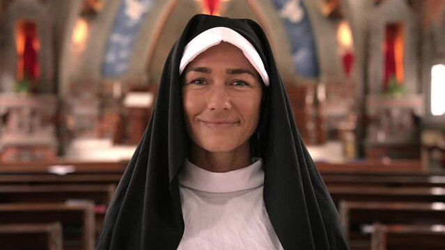 Woman Nun Looking at Camera While Standing Inside Church and Smiling. Portrait of a Young Adult Person Close up to Faith and Prayer. Standing in Church Between Rows. Catholic Church Servant Indoor 4k
