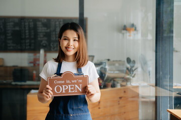 Young female hanging a welcome sign in front of a coffee shop. Beautiful waitress or hostess...