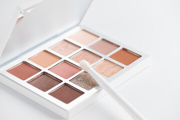 Eye shadow palette in nude beige shades with brush on a light background.