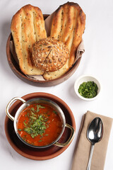Vegetarian tomato soup with herbs and bread on a table.