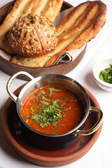 Vegetarian tomato soup with herbs and bread on a table.