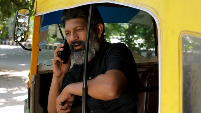 An auto-driver talking on phone during his rest time - lifestyle of an auto driver  public transportation  metro city. A man sitting his yellow and green cng auto - green transportation  pollution-...