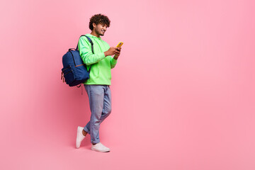 Full body photo of student arabian guy wear green sweatshirt browsing social media in smartphone isolated on pink color background
