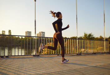 Young woman jogging on quiet summer morning. Confident slim energetic female athlete in sports suit...