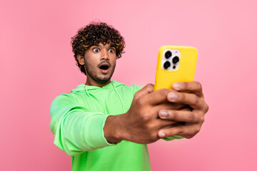 Photo crazy amazed young guy curly haired indian blogger holding mobile phone shocked how fast his device isolated on pink color background