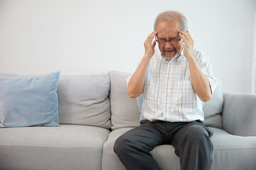 senior asian man suffering from headache on sofa