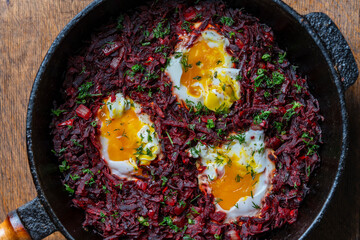Boiled red beets with fried eggs, red peppers, onions and green dill in a frying pan on a wooden...