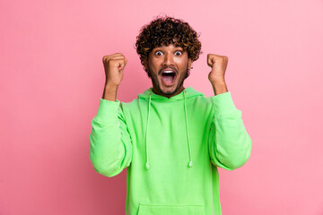 Photo of young funny indian guy curly hair model in green sweatshirt raised fists up football team fan isolated on pink color background