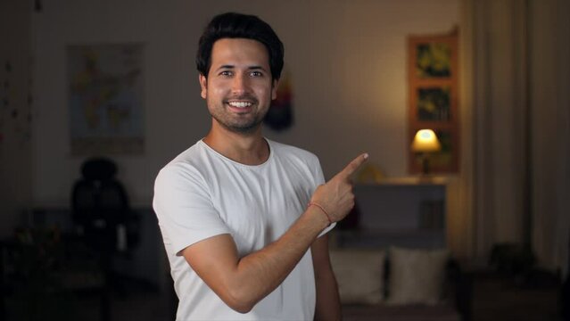 A man pointing fingers at the copy space at home - advertisement concept. A young smiling man pointing his index finger at something that stands out - a space for writing text