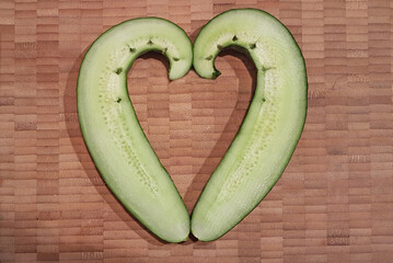 Crooked cucumber, cut in half and placed in a heart shape. Wood background