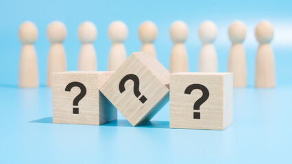three wooden cubes with question marks are placed on a blue table amid wooden figurines, representing business and education. the close-up focuses on the cubes