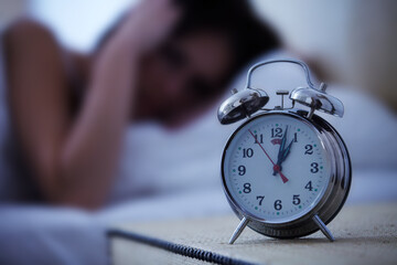 Alarm, clock and frustrated woman in a bed with hands on ears for noise, sound or alert at home. Time, bell and female person in a bedroom blur with fatigue, burnout or sleeping late from insomnia