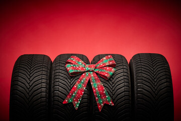 Car tires, new tyres, winter wheels isolated on red christmas background with bow ribbon present.