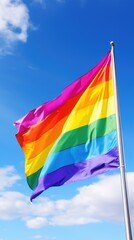 Rainbow pride flag waving in the wind on a vertical background of blue sky with clouds