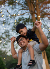 Portrait of happy Asian father giving son piggyback ride on his shoulders and looking up