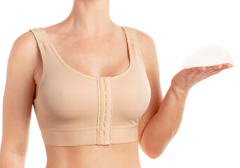 Woman wearing compressing bra, holding breast implant isolated on white background