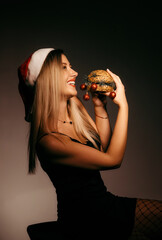 A beautiful girl in a Santa Claus hat eats a sandwich with New Year's decorations