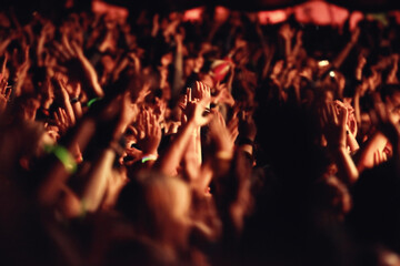 People, hands and crowd for music, festival and outside with arms raised for dancing, movement or enjoyment. Audience, concert and excitement with dj, band or singer with red, lighting and equipment