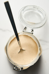 Tarator - Lebanese sauce from tahini with garlic, lemon juice and water. White or cream colored sauce in a jar on a marble background