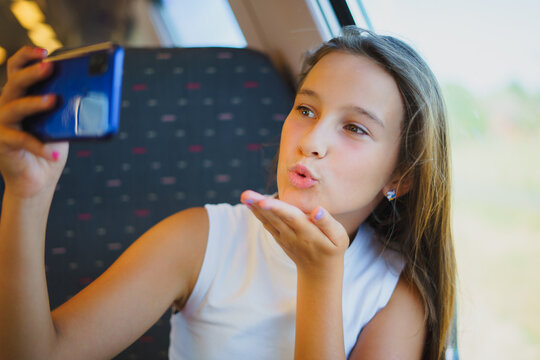 Little smiling girl travels by train while communicating via video conference on phone, takes selfie photo with air kiss