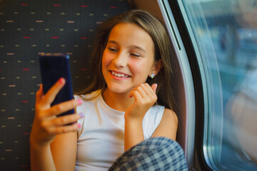 Little smiling girl travels by train while communicating via video conference on phone, takes...